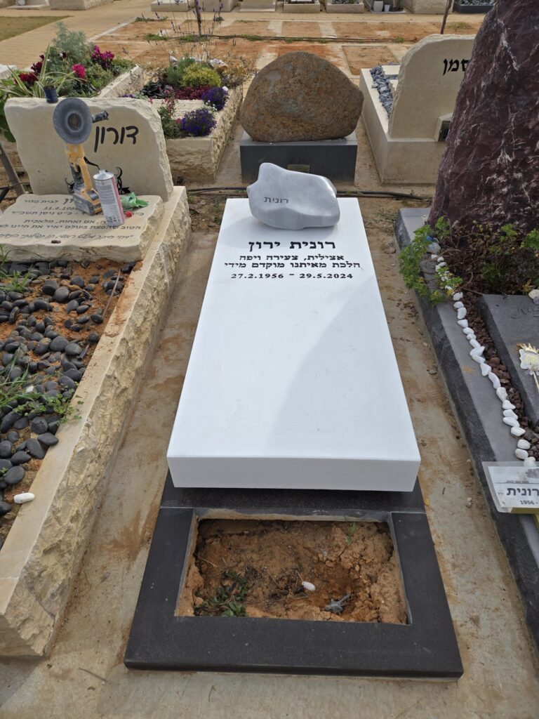 מצבה עשויה שיש לבן בעיצוב אמנותי ומינימליסטי, עם אבן טבעית מעוגלת המשמשת כפריט דקורטיבי, מתאימה לאזור השרון.