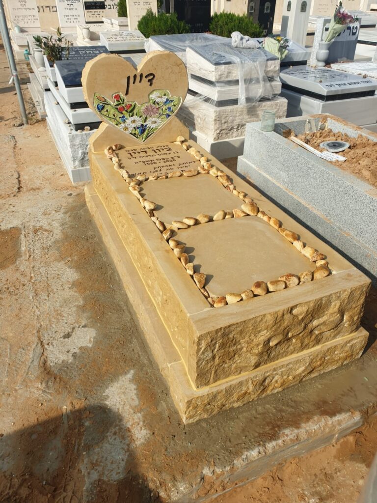 מצבת אבן חברון בגוון זהוב חם עם ראש בצורת לב ופסיפס צבעוני, מוקפת באבני נוי בהירות בדרום הארץ.